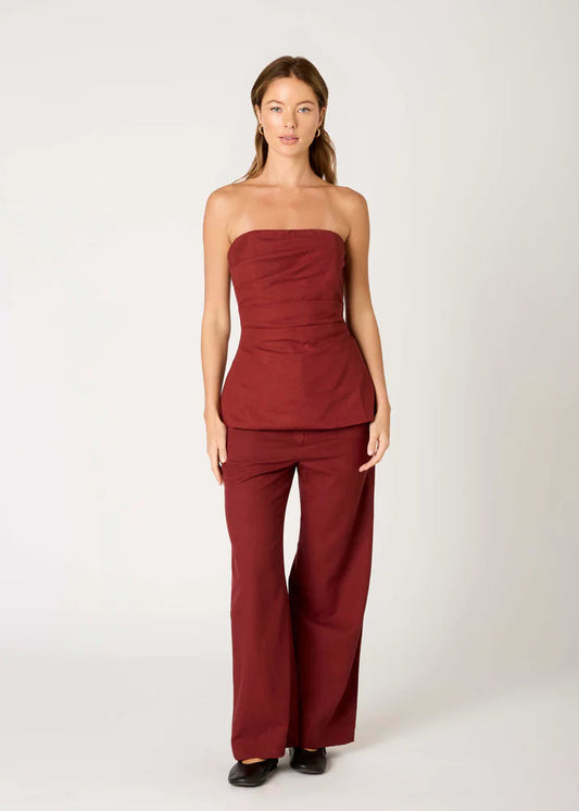 Woman wearing a strapless burgundy top and wide-leg pants on a white background