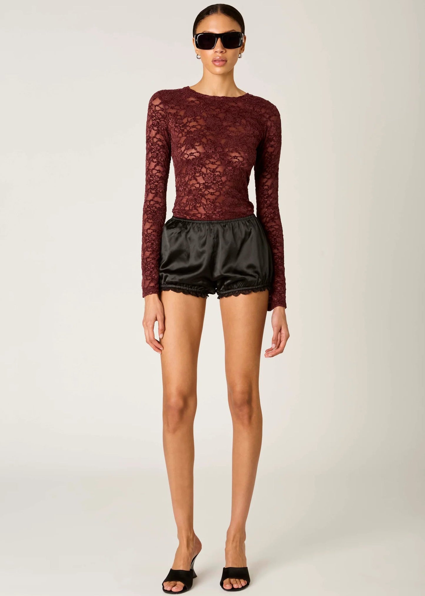 Woman wearing a burgundy lace top and black shorts on a white background