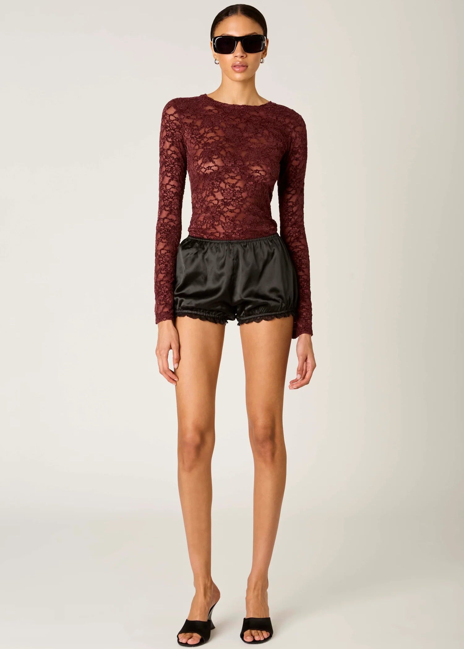 Woman wearing a burgundy lace top and black shorts on a white background