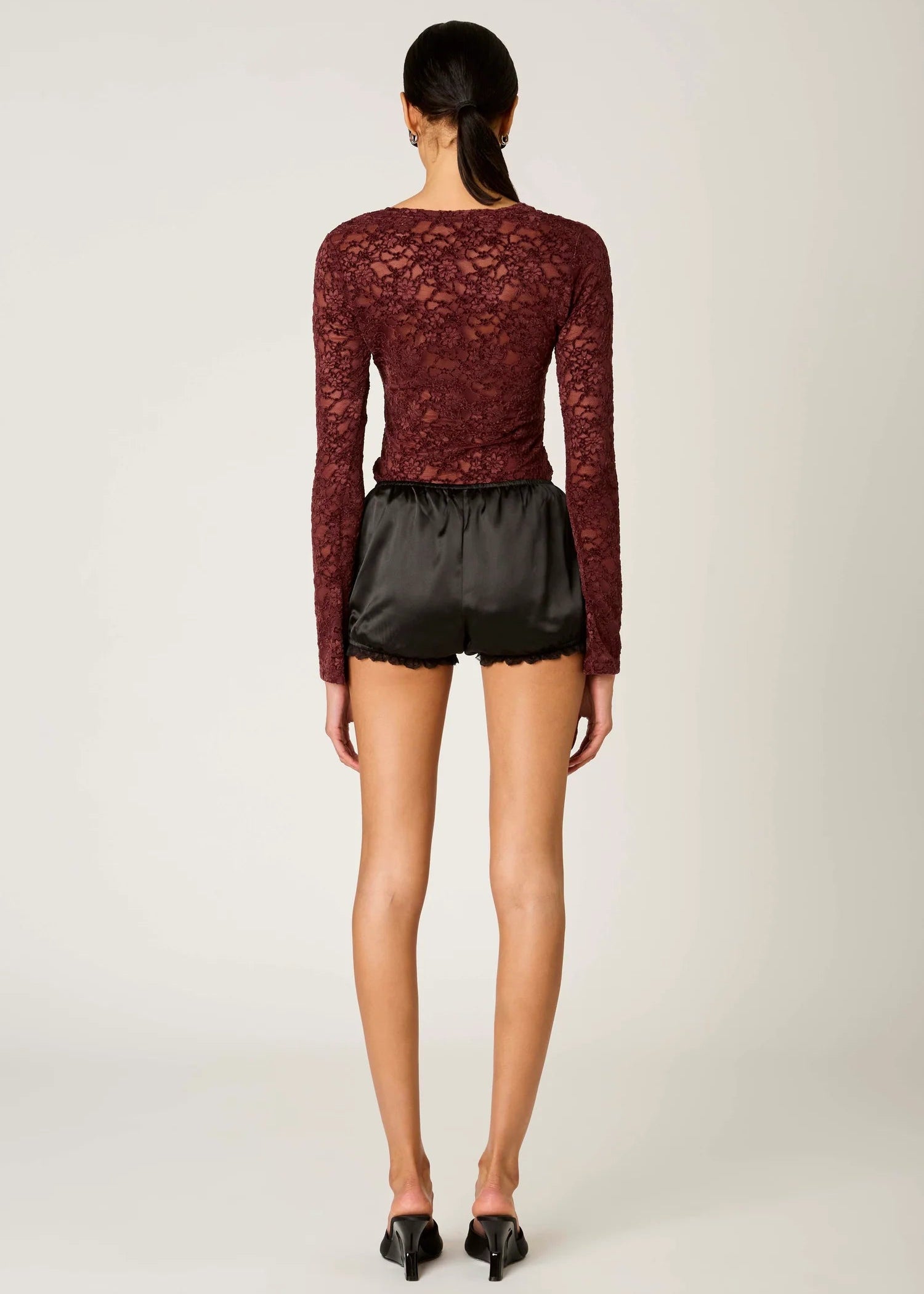 Model wearing a burgundy lace top and black shorts on a plain background
