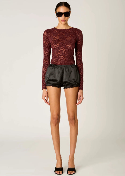 Woman wearing a burgundy lace top and black shorts on a white background