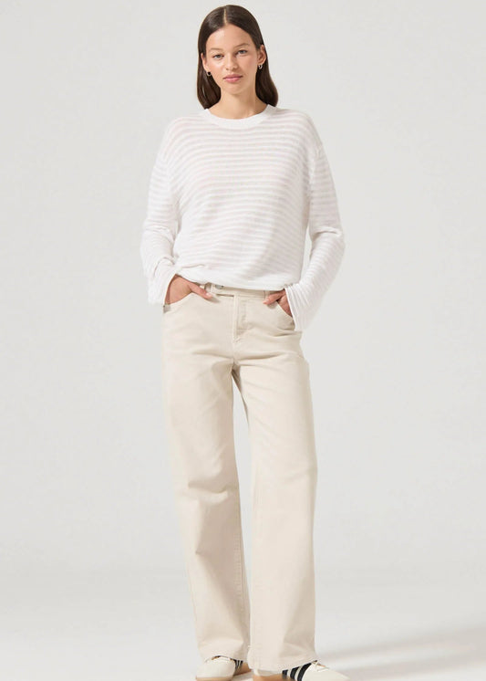 Woman wearing a white striped sweater and beige pants on a plain background
