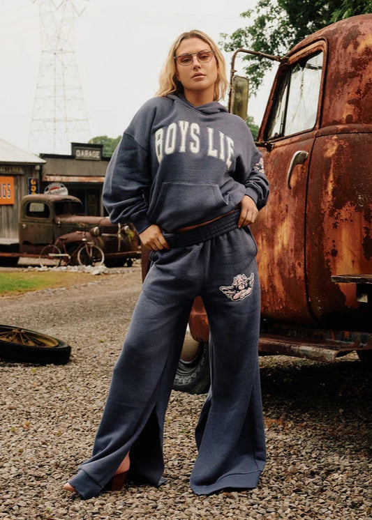 Person wearing a 'BOYS LIE' sweatshirt and pants in front of a rusted truck.