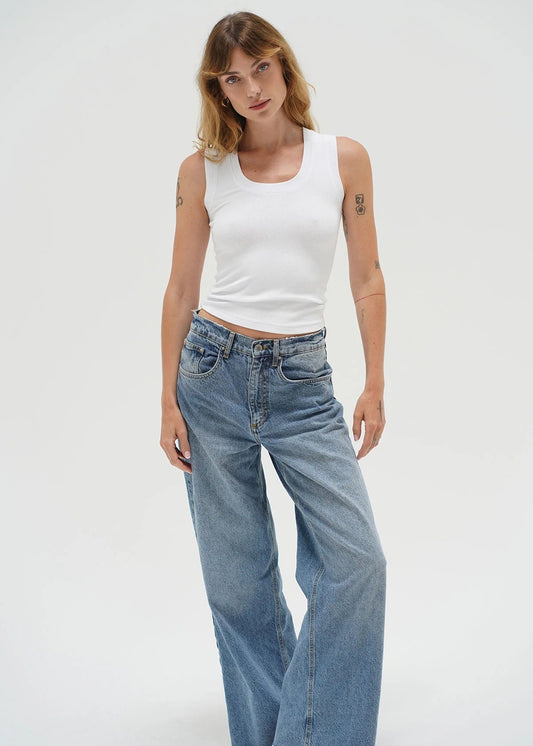 Woman wearing a white tank top and blue jeans on a white background. LNA Clothing