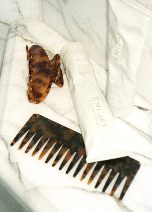 Tortoiseshell comb and hair clip on a white towel with 'EMILY' branding.