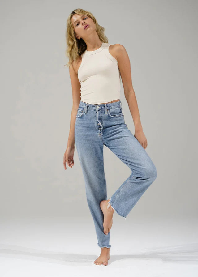 Woman wearing a white sleeveless top and light blue jeans on a plain background