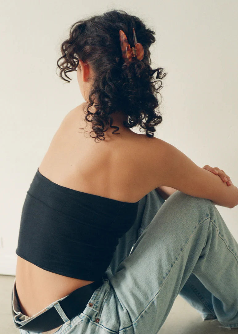 Person sitting with back to camera wearing a black strapless top and light blue jeans.