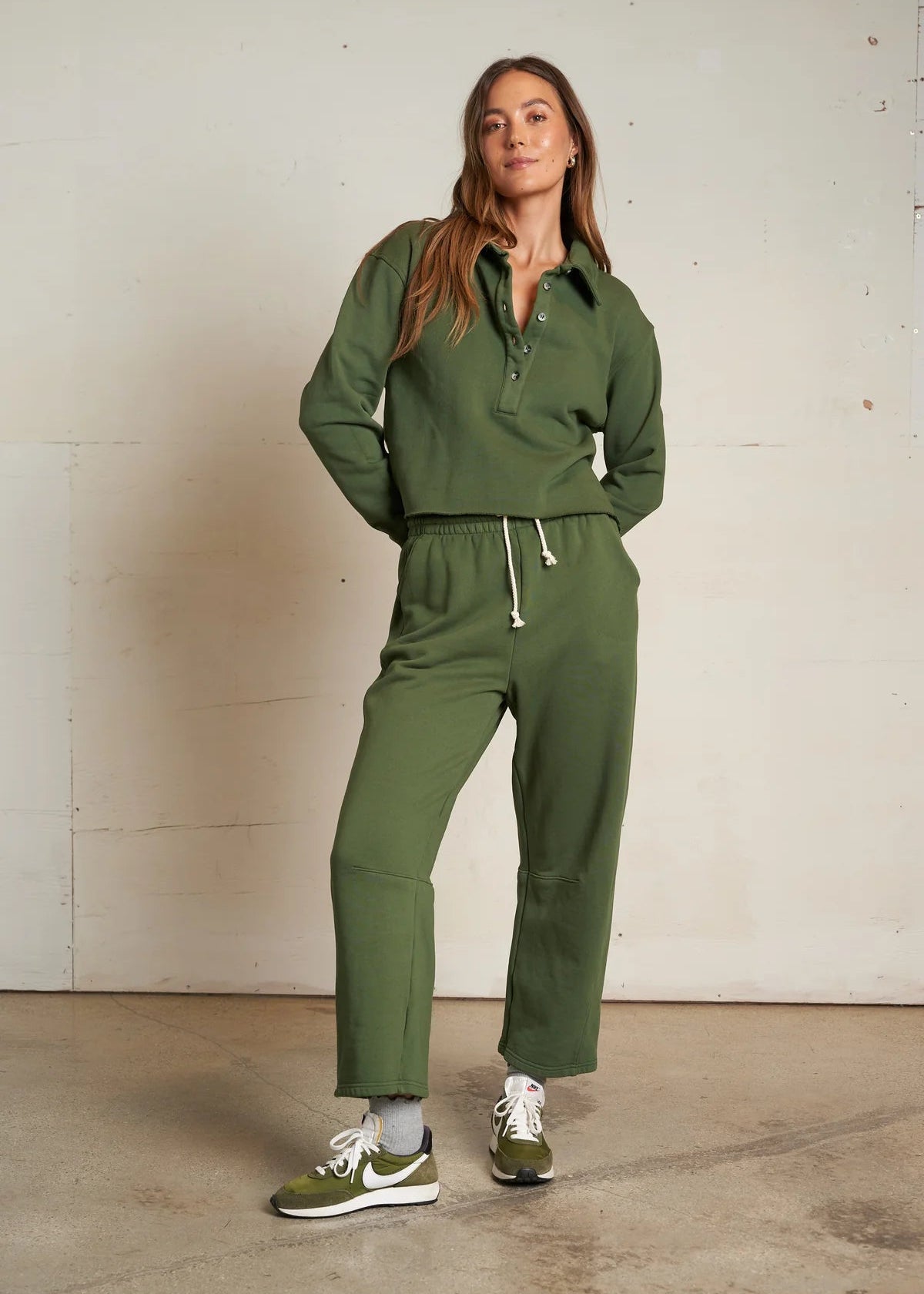 Woman wearing a green tracksuit standing against a plain wall.