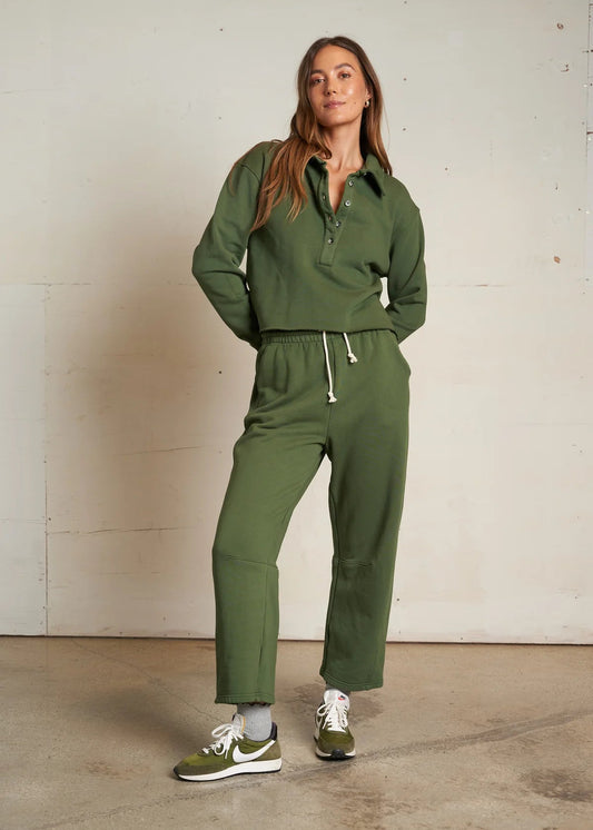 Woman wearing a green tracksuit standing against a plain wall.