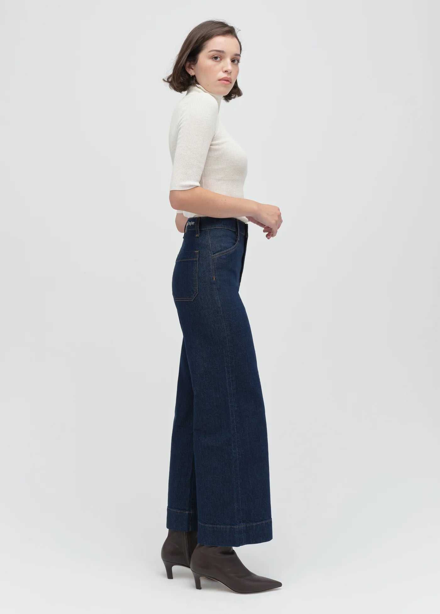 Woman wearing a white top and dark blue jeans on a white background