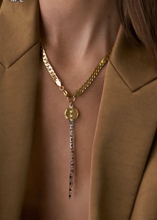 Gold necklace with a pendant worn by a person in a brown coat.