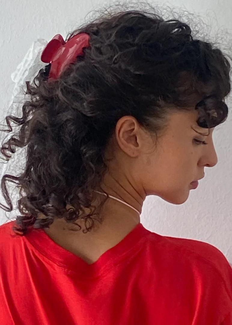 Woman with curly hair wearing a red headband and red garment against a white background