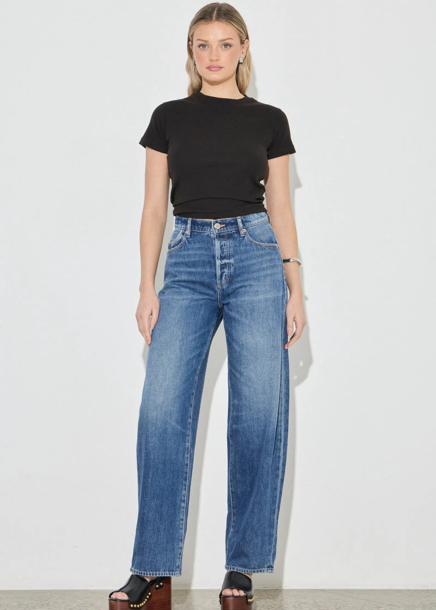 Woman wearing a black t-shirt and blue jeans on a plain background