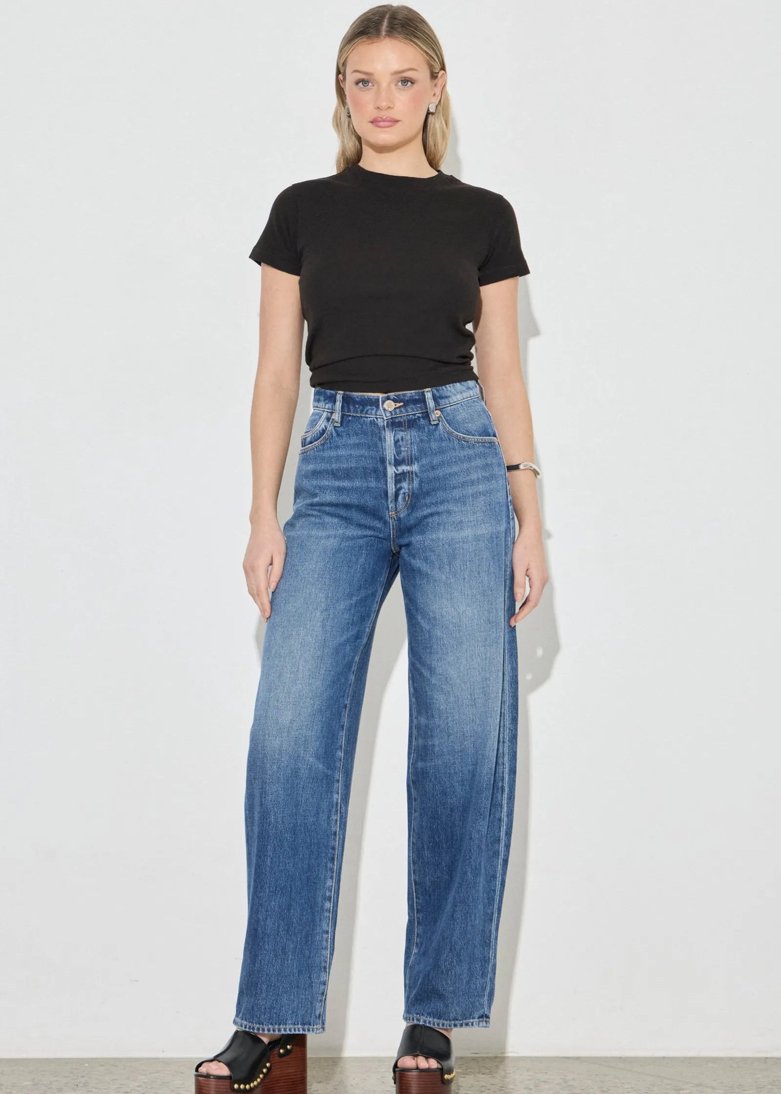 Woman wearing a black t-shirt and blue jeans on a plain background