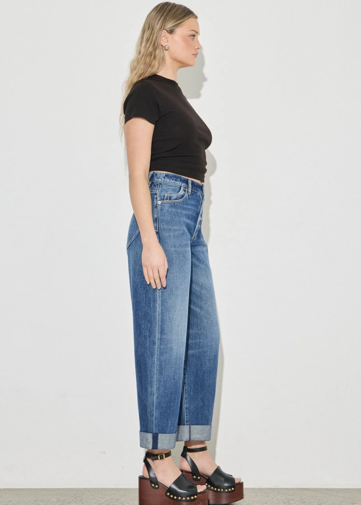 Woman wearing blue jeans and a black top against a white background