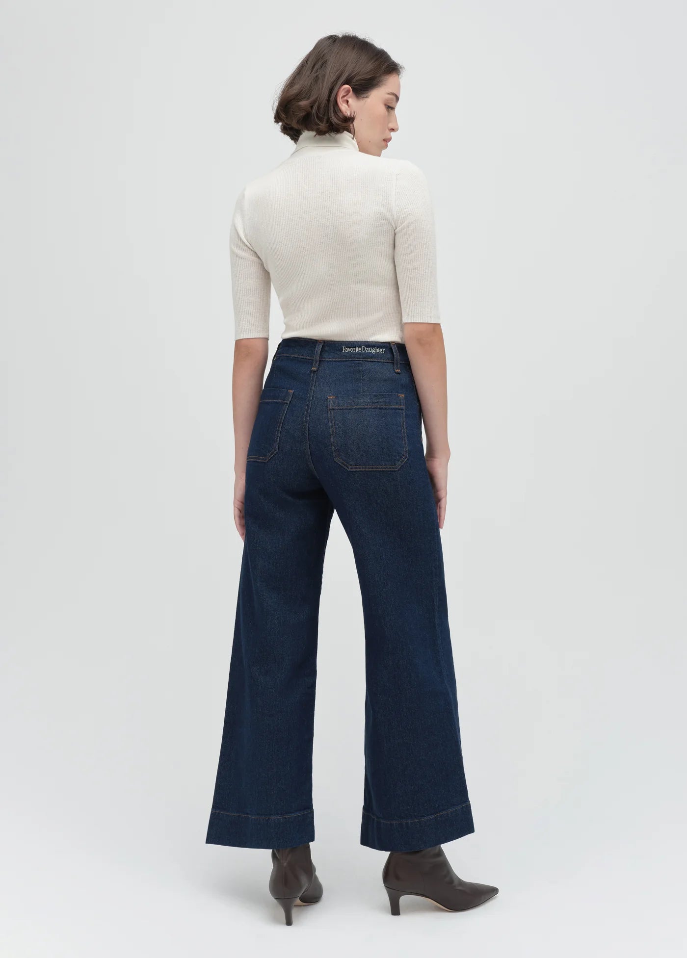 Woman wearing dark blue jeans and a white top on a white background